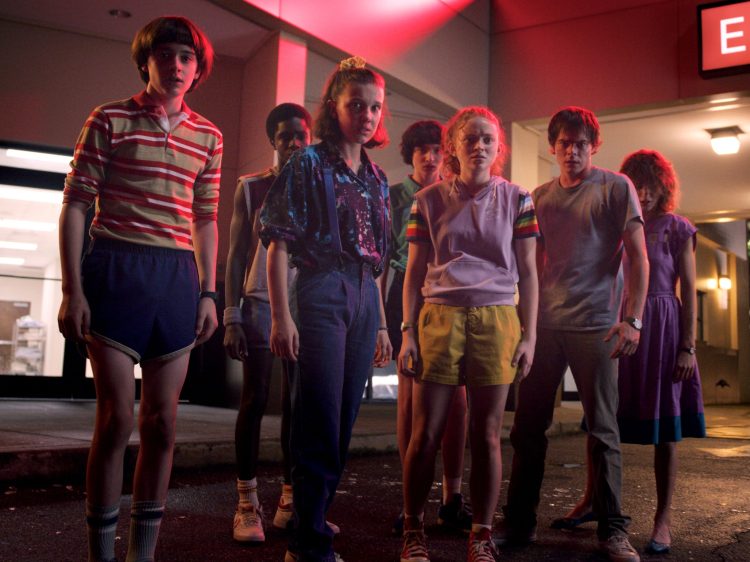 A still image from the third season of Stranger Things, showing the gang looking very concerned in a mall-like setting.