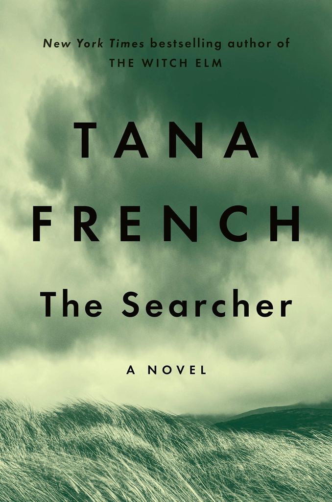 The cover to The Searcher by Tana French, which shows a landscape in a gloomy sort of gray-green color, featuring darkening clouds and hills of long, waving grass.