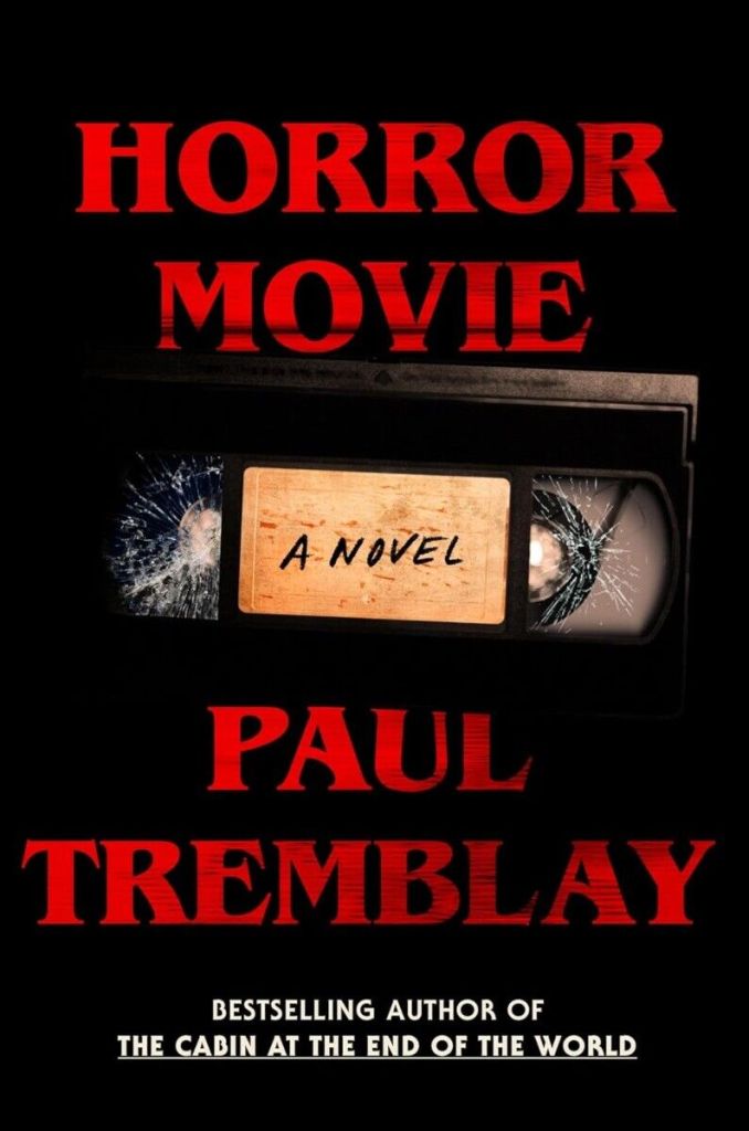 The cover to Horror Movie by Paul Tremblay, which features a black background and dark red text in the font of a 90s horror film. In the center is a VHS tape with its plastic windows cracked.